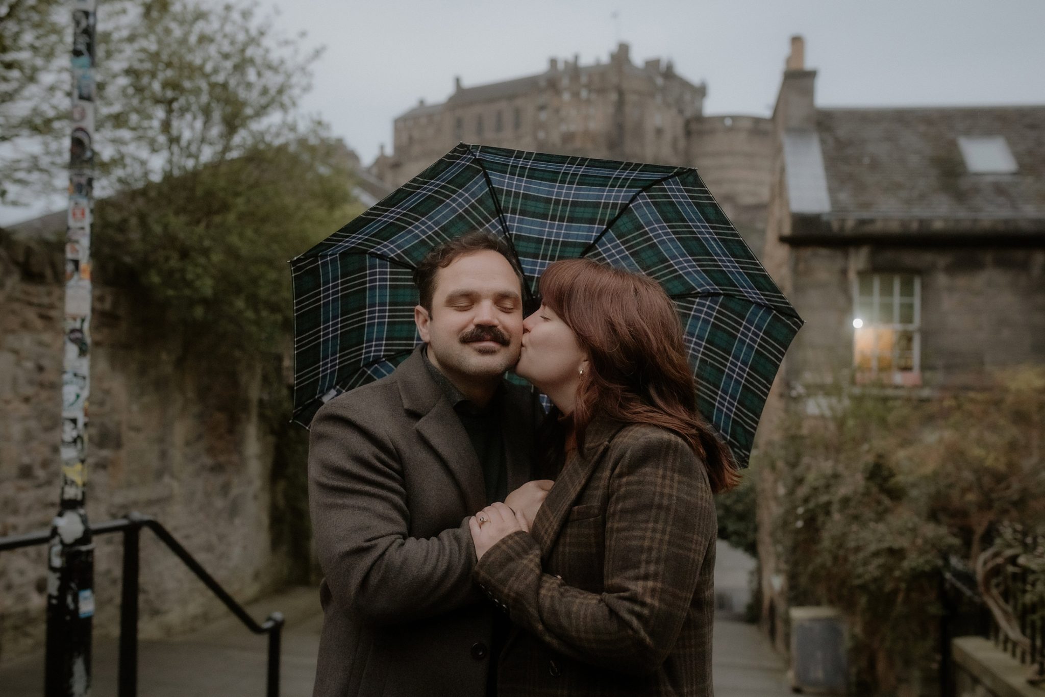 Just after she said yes — couple kissing on the cobbled Vennel Steps with Edinburgh Castle behind them. Edinburgh proposal photographer.