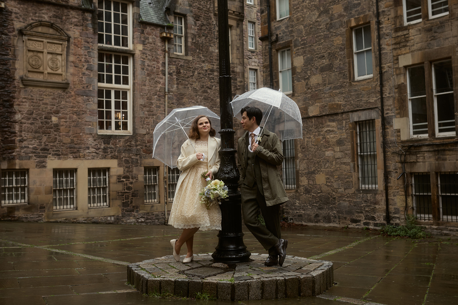 Couple walking through Edinburgh Old Town with umbrellas on their elopement day.
