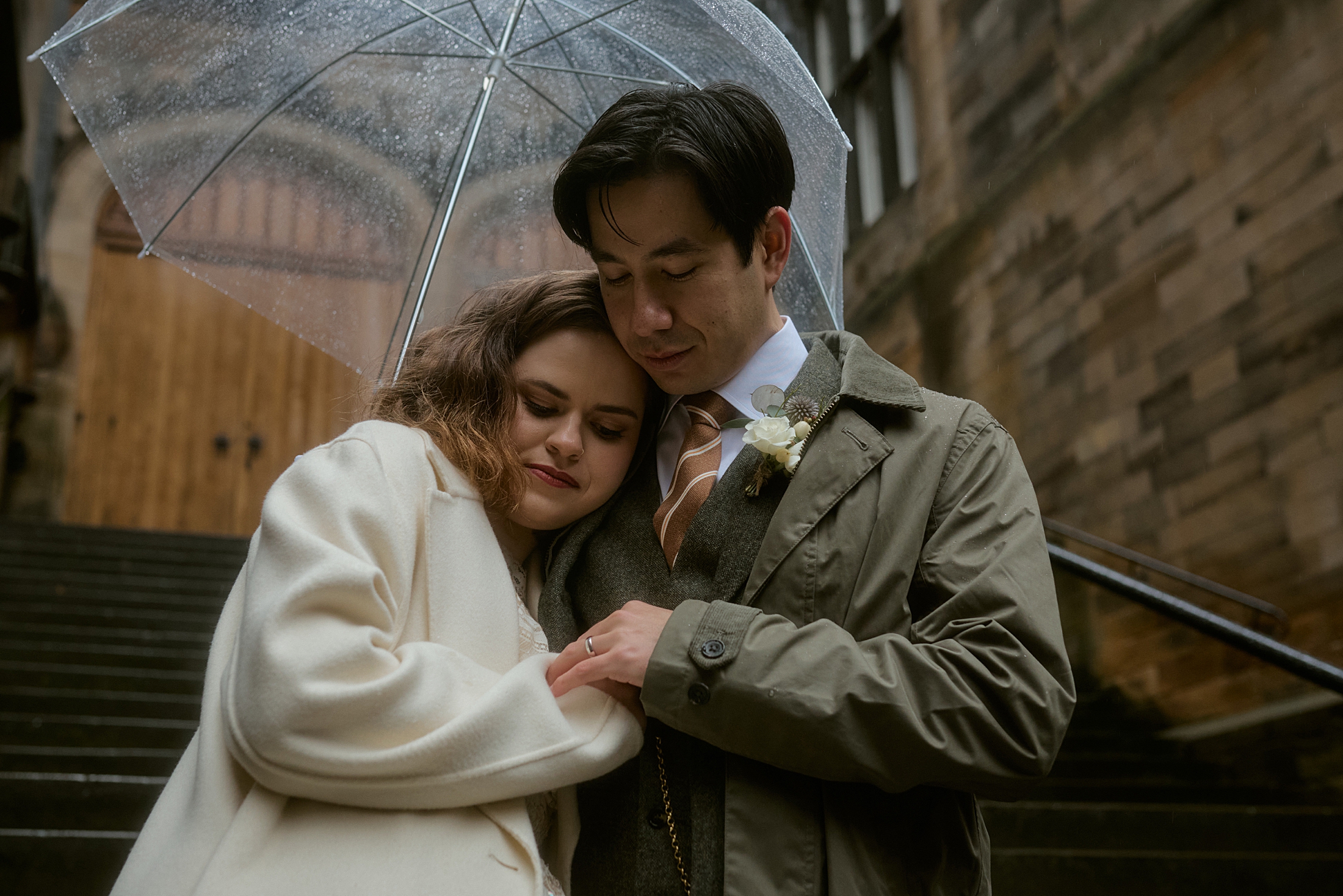 Couple embracing under umbrella in rain at New College courtyard in Edinburgh