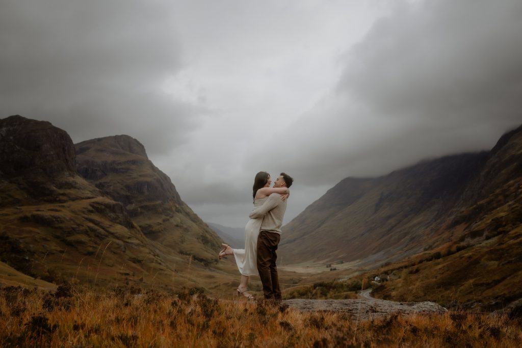Couple embracing in dramatic Glencoe landscape after a surprise proposal