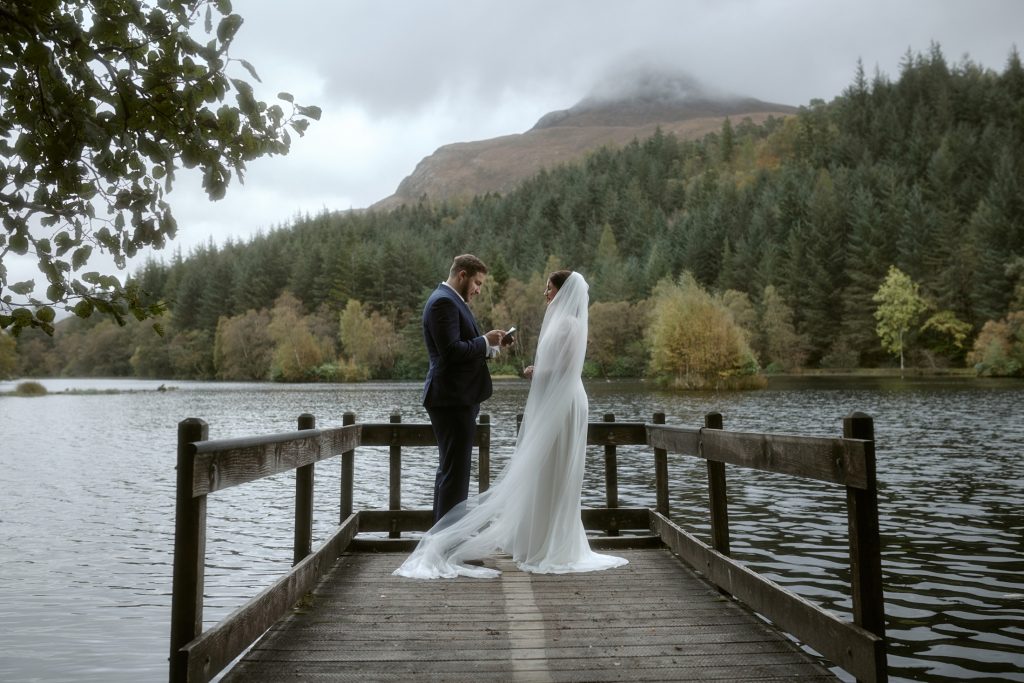 Couple exchanging vows on wooden jetty during Glencoe Lochan elopement in the Scottish Highlands