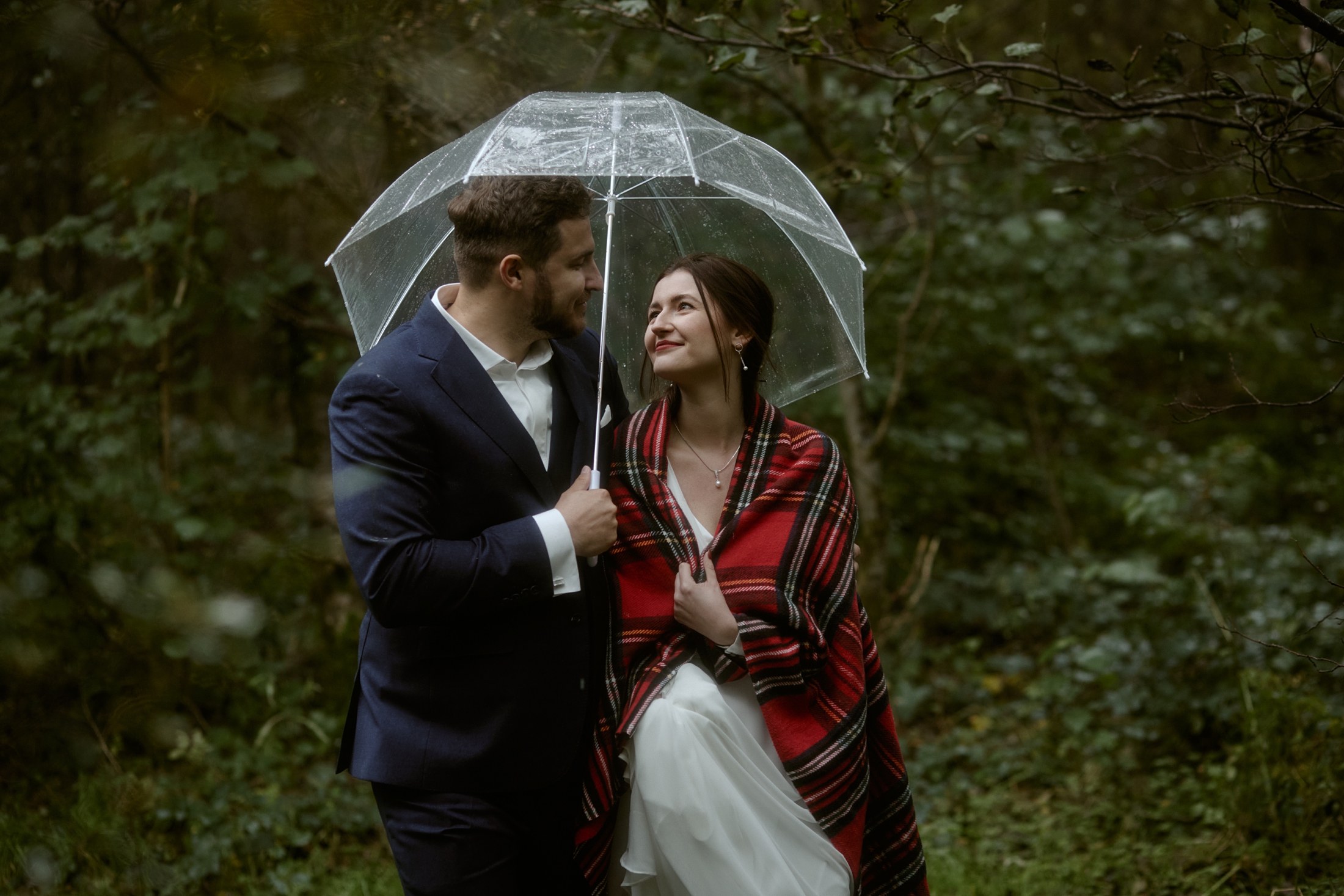 Couple under umbrella during rainy Glencoe Lochan elopement in the Scottish Highlands