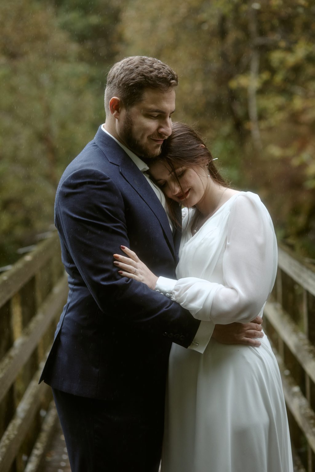 Couple having a cuddle in the rain during Glencoe Lochan elopement in autumn
