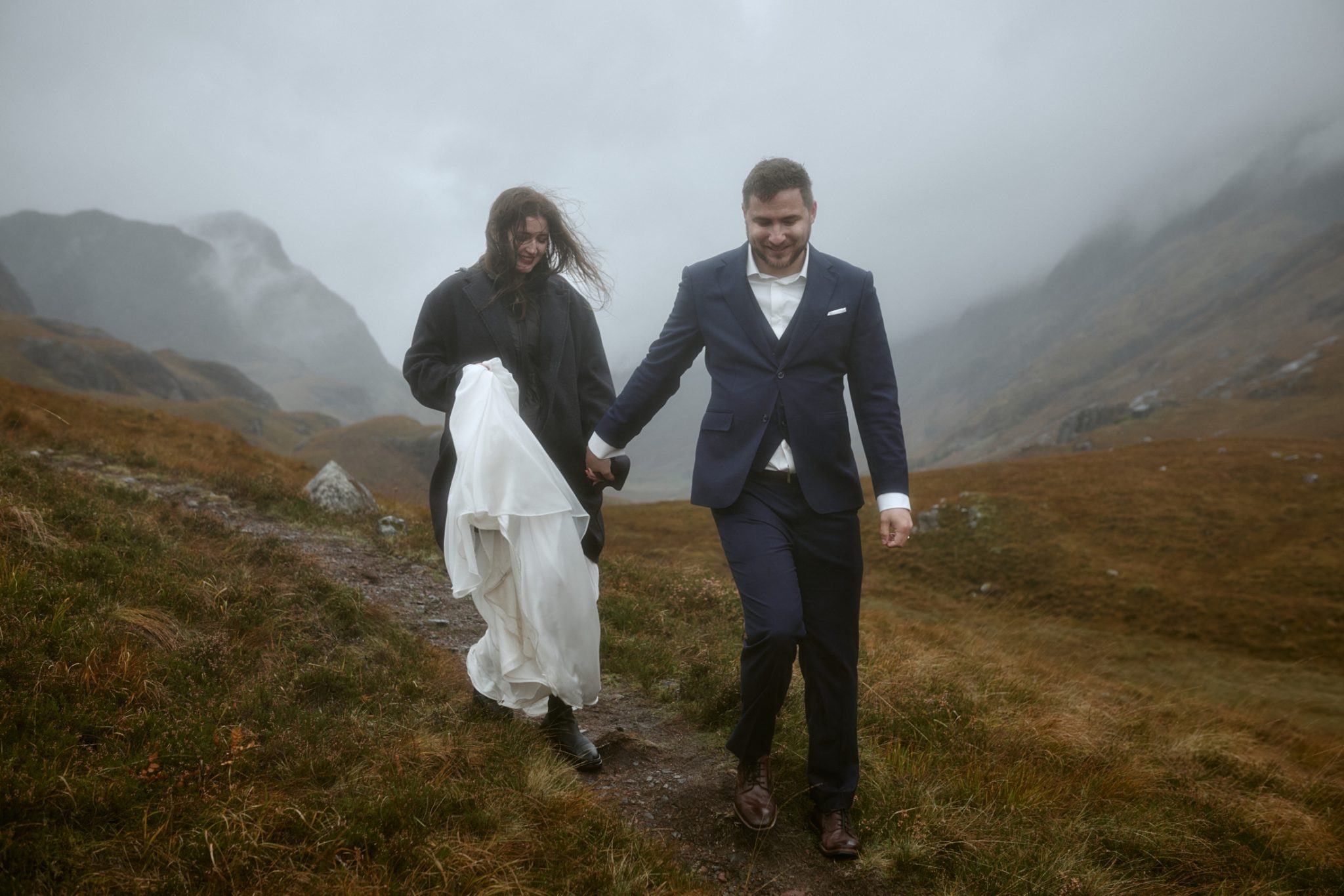 Couple walking hand in hand through misty Glencoe during elopement in Scotland