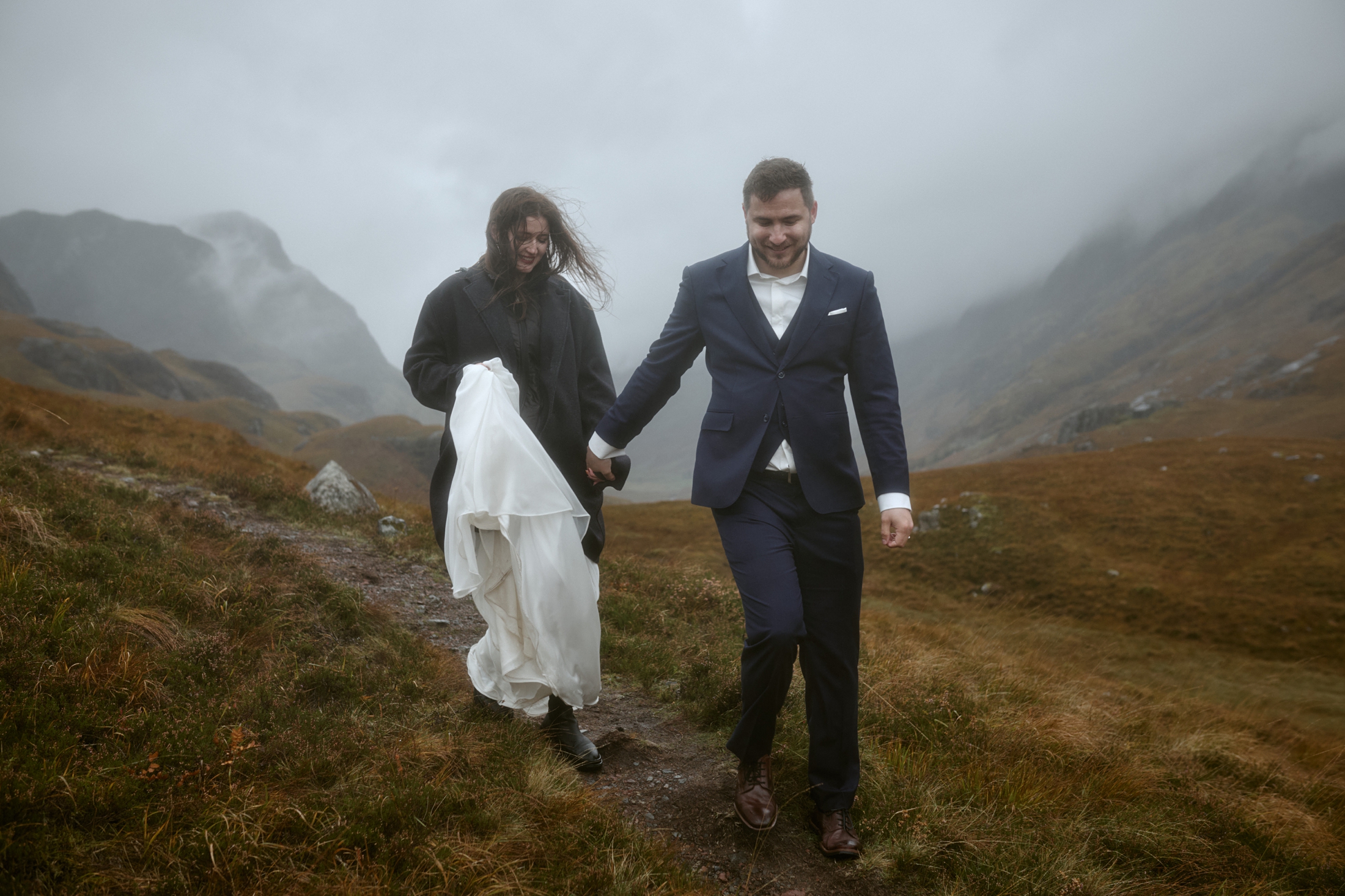 Couple walking hand in hand through misty Glencoe during elopement in Scotland