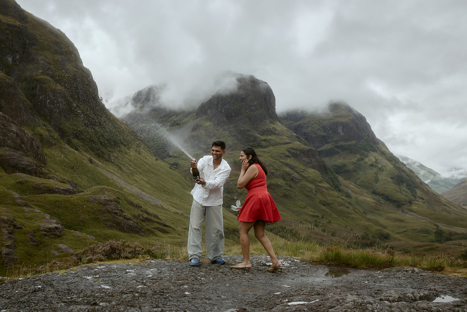 `Couple celebrating with champagne after surprise proposal at Three Sisters Glencoe Scotland`